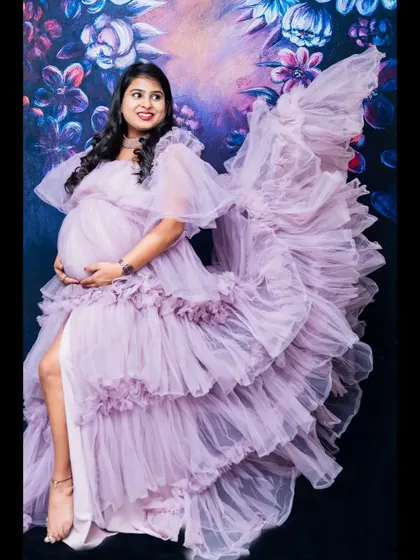 A work of art. The mom-to-be, in a stunning ruffled lavender gown, is posed against a painted floral backdrop, creating a dreamy and artistic portrait.