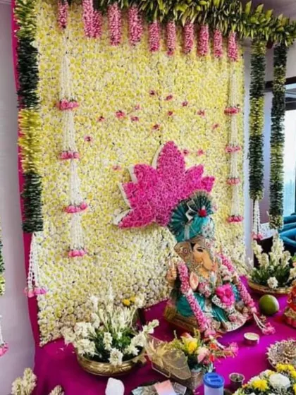 This vibrant Ganpati decor uses a backdrop of yellow and white flowers, accented with a pink lotus motif. The hanging floral strings and green garlands add layers of color and texture.