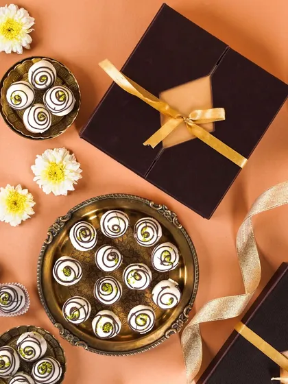 A flatlay of white chocolate pistachio truffles and their elegant gift boxes. The clean, minimalist composition with scattered flowers is both modern and festive.