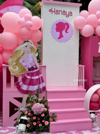 A life-sized Barbie cutout poses on a custom-built pink staircase, creating a perfect photo spot.