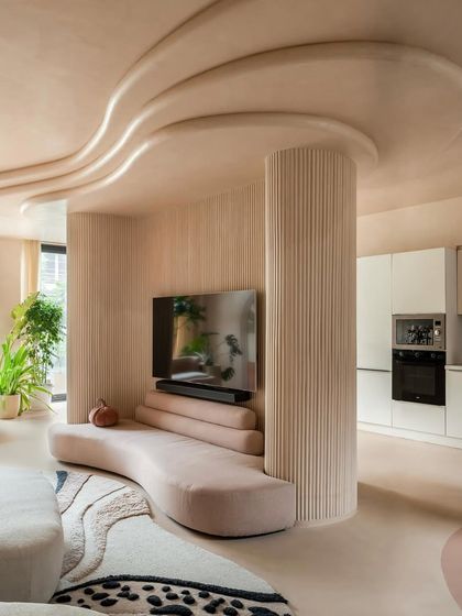 The wave-like forms in the ceiling, crafted from POP with a lime wash finish, create a sense of motion that flows down into the custom-designed curved sofa. This detail turns a structural column into a central design feature.