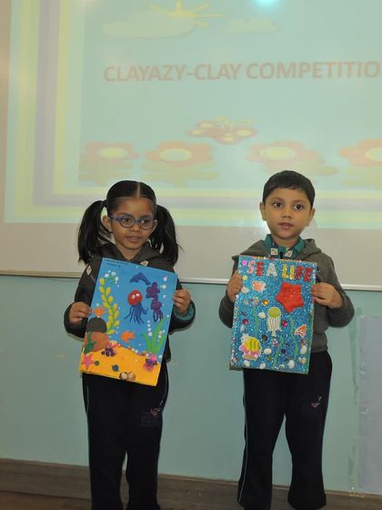 Two students hold up their colorful and imaginative clay art boards, displaying their hard work from the competition.