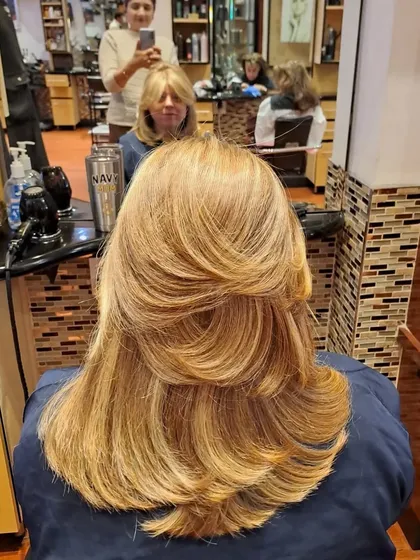 A layered blowout on blonde hair, showing how the style enhances color and dimension. The feathered layers around the face are a classic technique.