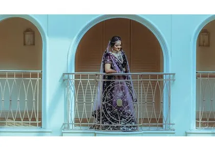 A wide shot of the bride on a balcony, looking like a queen in her castle. This type of grand portrait captures the full splendor of the bridal lehenga and the venue.
