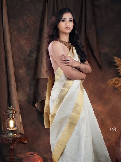 A modern interpretation of the traditional Kerala saree. The off-shoulder drape and the rustic studio setup with lanterns and pottery create a unique fusion of classic and contemporary styles.