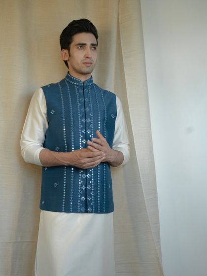 Draped in resplendent royalty, this blue jacket with intricate mirror work perfectly complements the elegance of a silk kurta and pajama.
