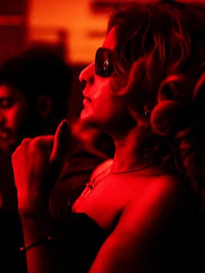 The dramatic red lighting at our events creates stunning visual moments. A guest is captured here, her profile illuminated as she enjoys the set.