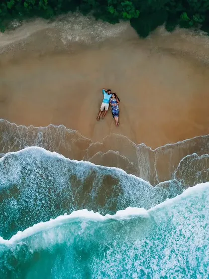 An aerial drone shot of a couple on a secluded beach, showcasing a unique perspective on their pre-wedding shoot. We use advanced techniques to create visually stunning and creative images.