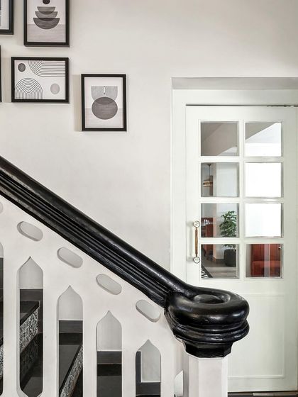 A close-up of the staircase's restored handrail shows the deep, polished black finish. Above it, a gallery wall of minimalist art adds a contemporary layer to the historic architecture.