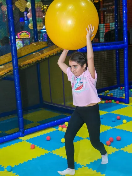 A girl engages in active play with a large yoga ball, part of the fun included in our seasonal offers.