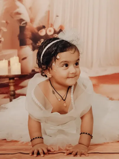 An angelic portrait of a baby girl in a white tulle dress, crawling in a beautifully styled bohemian-themed set with pampas grass and candles.
