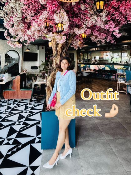 A full view of my birthday outfit in a beautiful cafe setting. The soft blue jacket and tan shorts are elevated by the vibrant pink bag, creating a chic and balanced look perfect for celebrating.