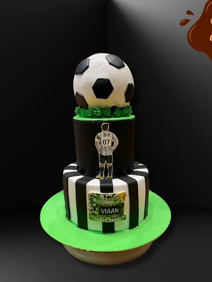 A two-tier football theme cake perfect for a young sports fan. The design includes a striped bottom tier, a player cutout, and a realistic fondant football on top.