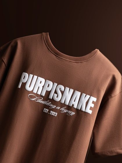 A clean, angled shot of the t-shirt, focusing on the neckline and the bold branding. The lighting is soft and even to show the true color of the fabric.