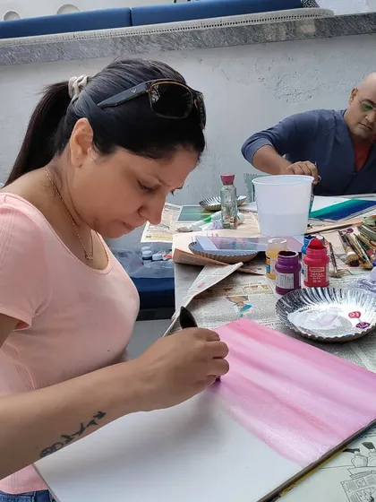 An adult student focused on creating the perfect sunset sky for her sailboat painting, carefully blending shades of pink and purple.