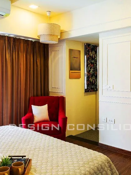 A simple and elegant bedroom with a pop of color from a red accent chair. The wall moldings add a classic touch, while the large window lets in plenty of natural light.