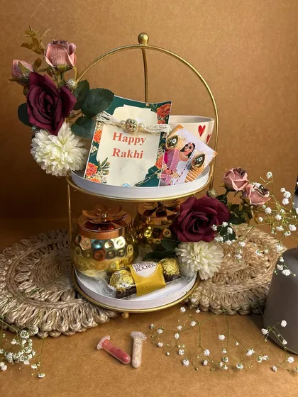 A royal treat for Bhaiya and Bhabhi this Rakhi. This two-tiered hamper includes a personalized photo, chocolates, and traditional roli-chawal, all beautifully decorated with flowers.
