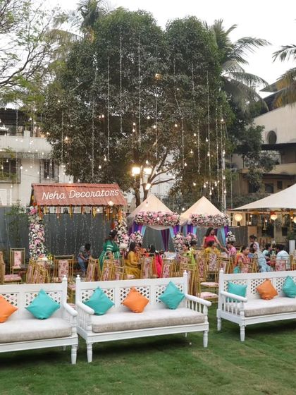 A wide shot of the festive lawn setup for a Mehendi. The combination of string lights, decorative tents, and pops of color from the cushions creates a lively and inviting atmosphere.