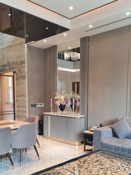 A luxurious living and dining area where a large mirror enhances the sense of space. The use of cool grays, metallic accents, and textured walls creates a sophisticated and modern environment.