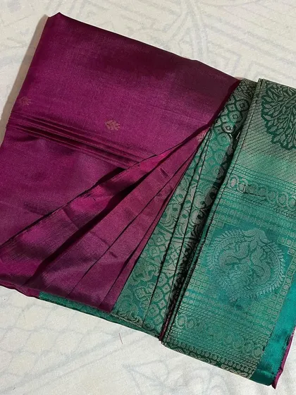 A rich magenta saree with a contrasting teal border, folded to display its unique design.