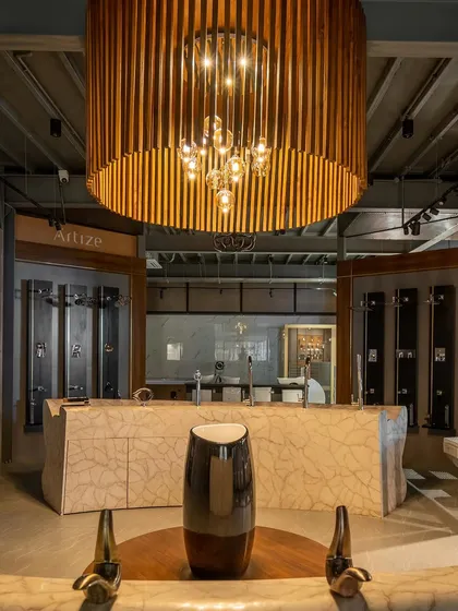 Inside the Satyam showroom, a large, custom chandelier made of wooden slats hangs over a marble-clad display counter. This central feature adds a touch of warmth and sophistication to the industrial interior.