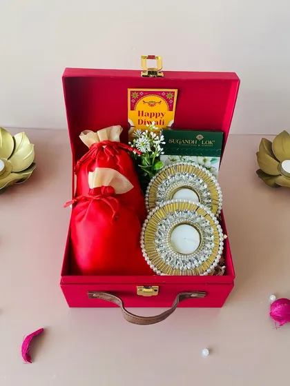 A beautiful shot of the red suitcase hamper, perfect for Diwali gifting. The combination of the bright red box and the ornate T-light holders creates a truly festive feel.