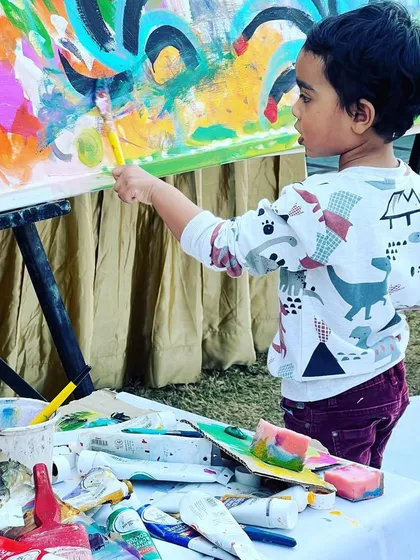 The best way to start an art workshop is to just dive in! A young participant adds his creative touch to a large community canvas at a family lunch gathering.