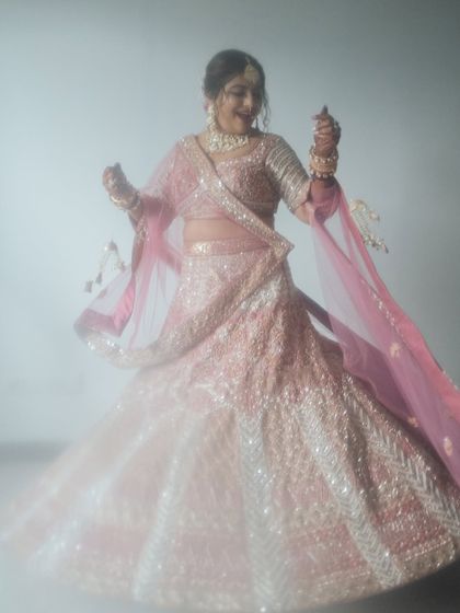 A dreamy, ethereal portrait of a bride in a pink lehenga. The soft focus and her twirling motion create a magical and romantic image.