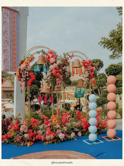 A playful installation for a Kite Carnival, with colorful stacked pots, floral arrangements, and hanging bells and tassels, creating a vibrant and festive photo corner.