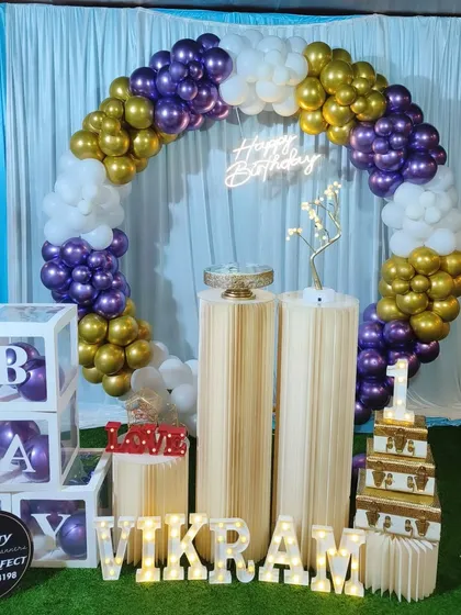 A striking birthday decoration featuring a purple, gold, and white balloon ring, set against a light blue curtain for a pop of color.