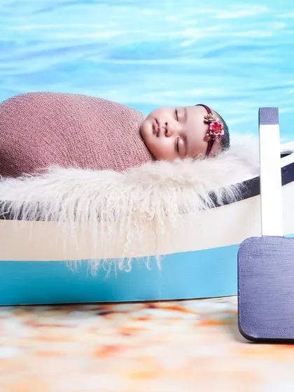 Setting sail on a new adventure with this nautical-themed photoshoot. The baby is safely swaddled in a miniature boat prop against a bright beach and ocean backdrop.