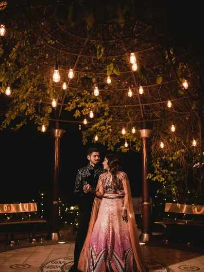 A romantic shot of the couple under a canopy of fairy lights. This image captures the magical, intimate ambiance of an outdoor evening reception.