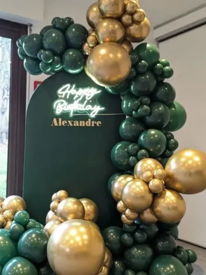 A luxurious balloon arrangement in dark green and gold. The 'Happy Birthday' neon sign and personalized name make this a very chic and custom setup for an adult birthday.