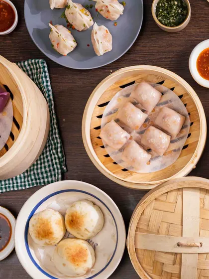 A top-down view of a diverse dim sum spread. You can see various types, from purple and pink steamed dumplings to pan-fried gyoza, showcasing the variety I offer for any gathering.