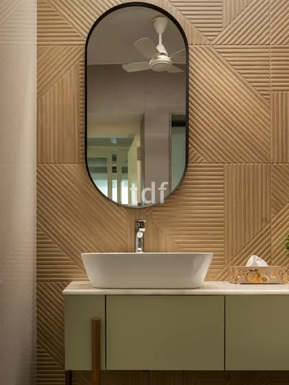 A detail of the clinic's powder room, where textured wall tiles in a warm wood tone create a sophisticated backdrop. The clean lines of the vanity and the elegant oval mirror contribute to a serene and modern aesthetic.