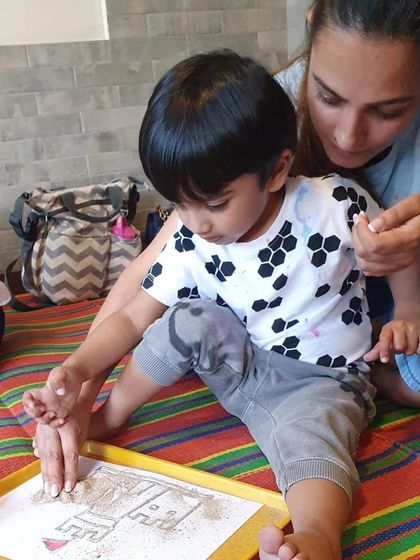 A parent helping her child with a sand art project. These activities are great for developing fine motor skills as they carefully pour sand onto their designs.