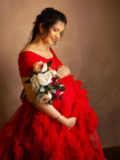 A close-up portrait focusing on the mother's gentle expression as she holds a bouquet and cradles her bump. The rich red of the gown adds warmth and love to the image.