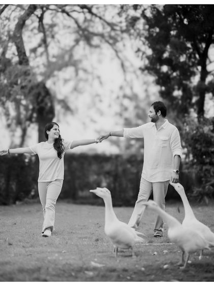 A fun and quirky black and white photo of a couple interacting with geese in a park. This spontaneous moment adds a touch of humor and personality to their pre-wedding gallery.