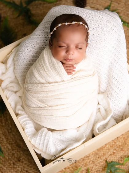 A rustic setup with a baby in a white wrap placed in a wooden box on a jute mat, accented with natural pinecones.
