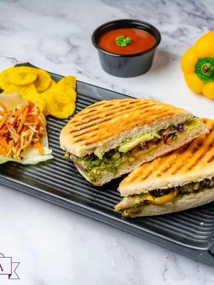 A freshly prepared Exotic Grilled Veggie Sandwich in panini bread. I use a medley of colorful vegetables like zucchini and bell peppers, grilled to perfection and served with a side of salad and chips.