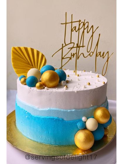 A modern blue and white ombre cake decorated with blue, white, and gold spheres and a dried palm spear for a chic, contemporary look.