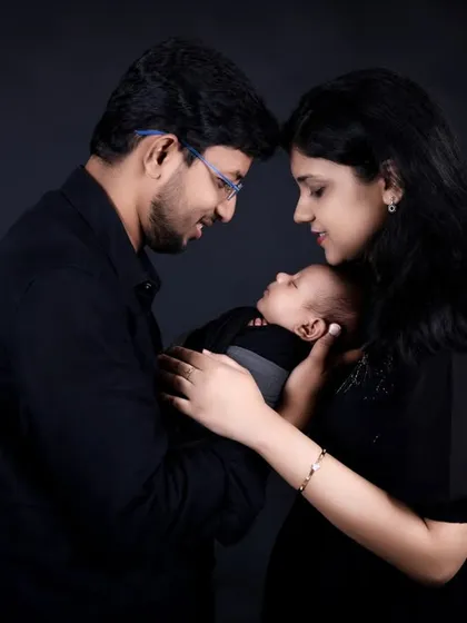 A classic family pose, with the parents looking lovingly at their new baby. The dark, simple background keeps the focus entirely on the family's bond.