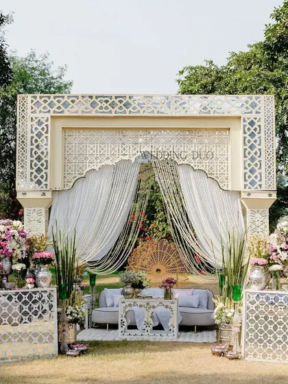 Sun-kissed simplicity meets royal elegance. This Haldi setup features an intricate ivory jaali backdrop, soft drapes, and bursts of pastel florals, creating a look of understated grace and cultural charm.
