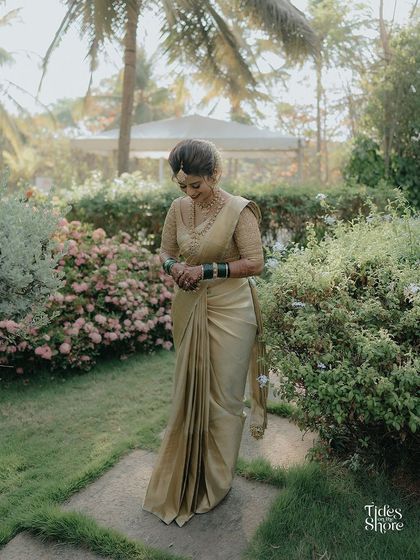 A solo shot of bride Sanghavi in her elegant gold muhurtham saree, captured in a beautiful garden setting.