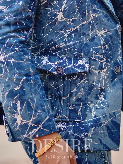 A detailed close-up of the blue splatter-print blazer, focusing on the custom buttons and functional pocket design. Every element is carefully considered.