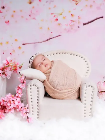 Even though the block says 'ONE', this image showcases a newborn-style pose. A peacefully sleeping baby is swaddled and placed on a miniature couch amidst a dreamy cherry blossom theme.