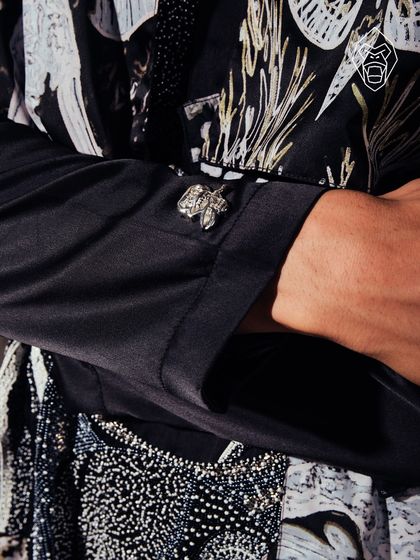 A detail of the Mythic Tapestry cuff, featuring a sculpted metal butterfly. This small detail adds a layer of symbolism and refined hardware to the folklore-inspired ensemble.