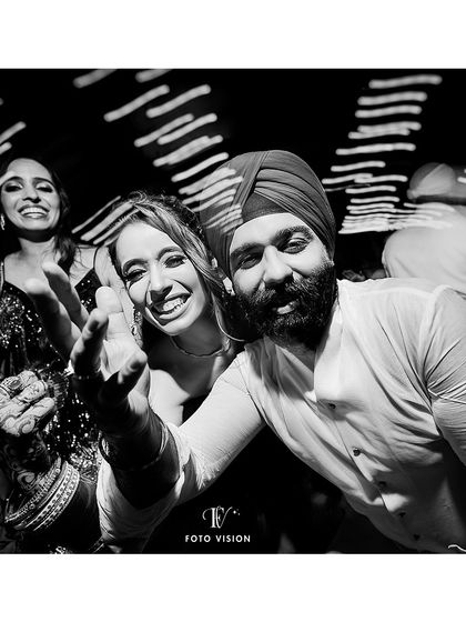 A fun, interactive moment on the dance floor. This candid shot shows the groom reaching out towards the camera, inviting the viewer into the celebration.