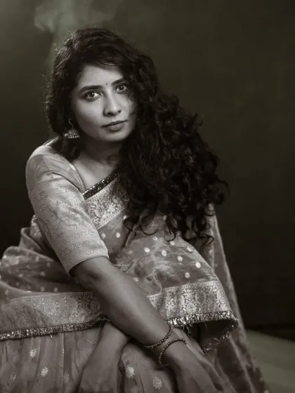A monochrome portrait of Vennela, wrapped in a beautiful saree. The black and white treatment emphasizes the rich textures of the fabric and the thoughtful expression on her face, creating a powerful and emotive image of strength.