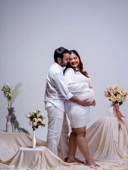 A tender embrace from behind, with the focus on their connection. The clean, simple setup with draped fabrics and flowers adds a touch of elegance to this classic couple maternity pose.